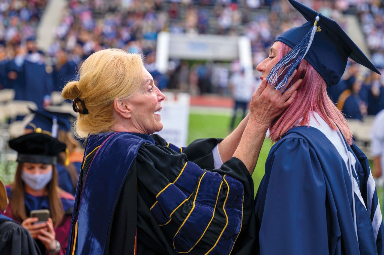 a smiling older woman touches the face of a younger Villanova graduate at commencement