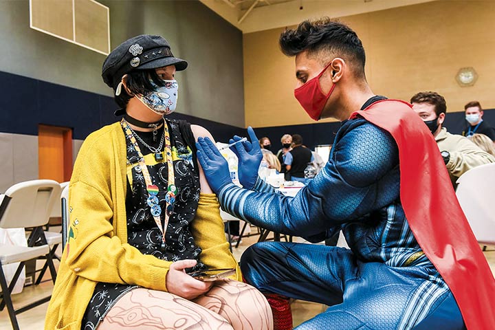Dr. Mayank Amin dressed in a superhero costume gives a COVID-19 vaccine to a seated woman