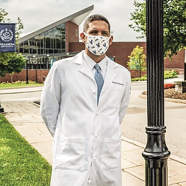 a man wearing a Villanova lab coat and Villanova face mask stands outside of Finneran Pavilion