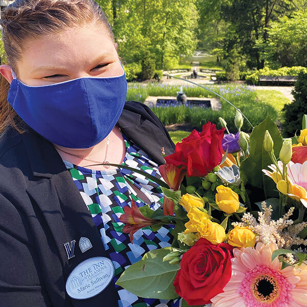 a woman wearing a blue face mask stands outside holding a bouquet of flowers