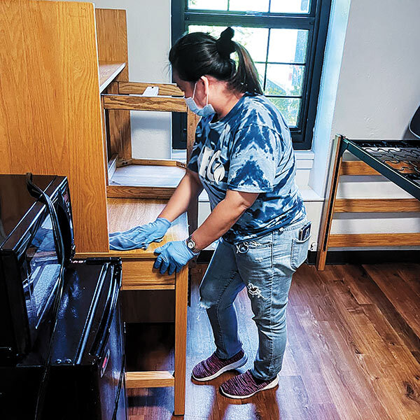 woman wearing gloves and a face mask cleaning a dorm room