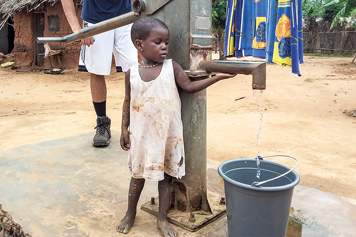 Young child in Ghana leaning against a handwater pump