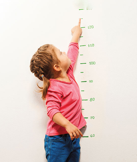 young girl in braids measuring her height on a wall chart