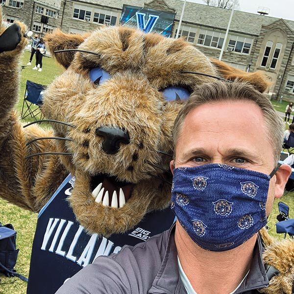Villanova mascot Will D. Cat stands with a paw on the shoulder of a man wearing a blue mask