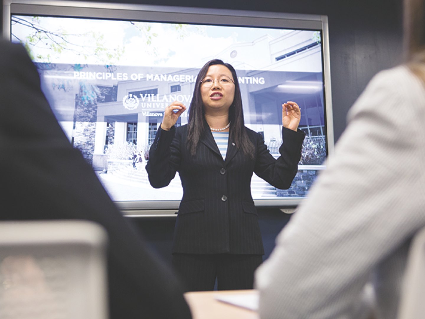 A female Villanova School of Business professor in a suit speaking to a classroom of students.