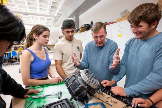 CSP183_20231025_343 Three students gather around a professor as he demonstrates an engineering concept.
