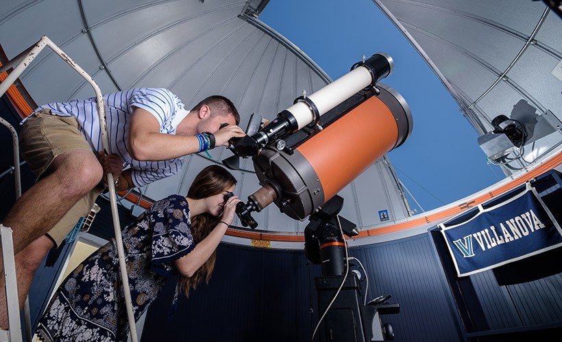 Two students look through a telescope in the observatory.
