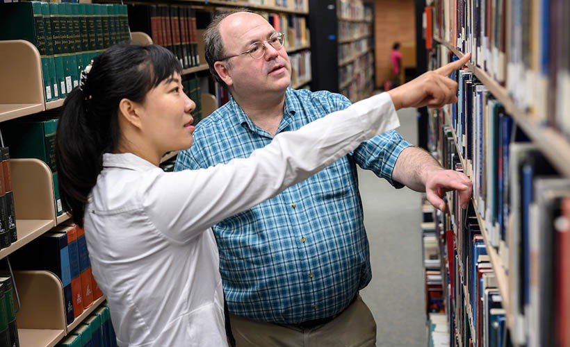 Student and research librarian look at books in Falvey Library.