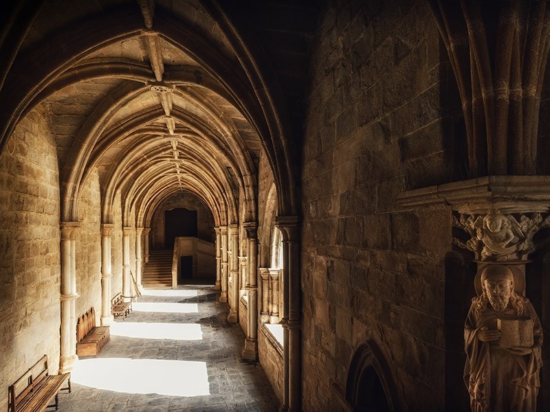 A photo of a row of cloisters with cathedral ceilings. Sun filters through the openings.