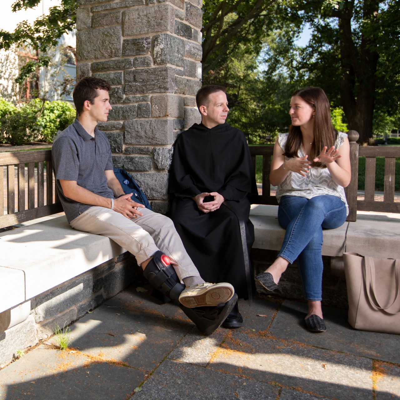 Father Kevin talks to two students in grotto