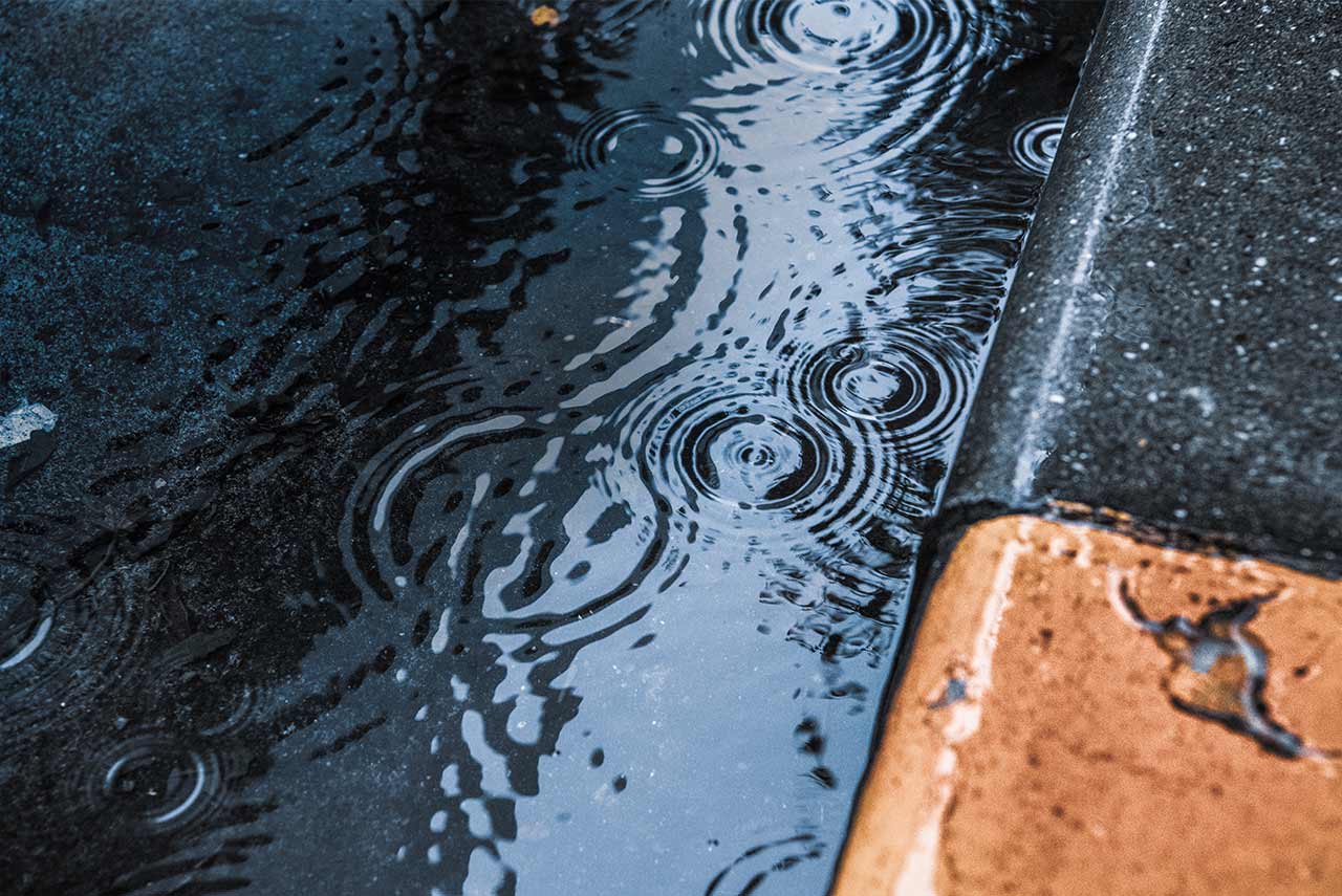 close-up of raindrops rippling in a puddle next to the street curb
