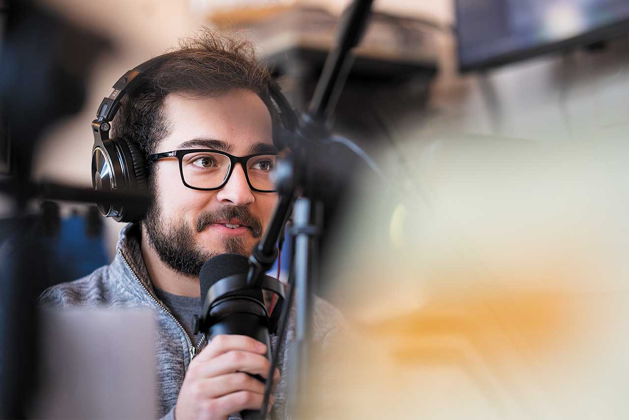 a male radio DJ wears a headset and speaks into the microphone