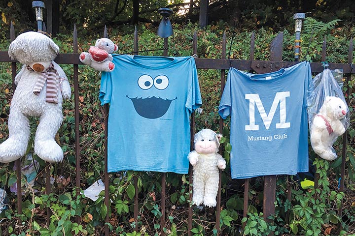 two blue t-shirts and four white stuffed bears hung outside on an iron gate